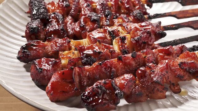 Close-up of Japanese yakitori chicken and green onion skewers on a plate, glazed with sweet soy sauce