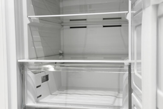 Clean empty white modern refrigerator interior with glass shelves and drawer