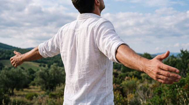 Man with arms outstretched embracing nature freedom concept in rural landscape under cloudy sky