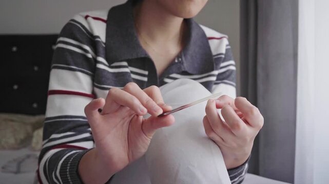 A woman sits by a window filing her nails during a quiet at-home manicure, emphasizing personal grooming, self-care, relaxation and everyday beauty maintenance