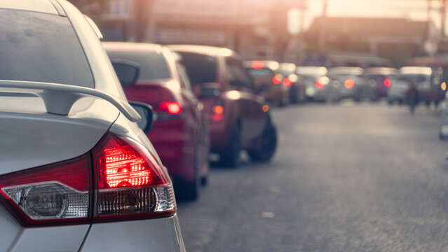 Rear view shot of a silver car waiting in heavy city traffic during the day. The bright red tail light is highlighted as multiple vehicles queue up on the road creating a busy commute scene.