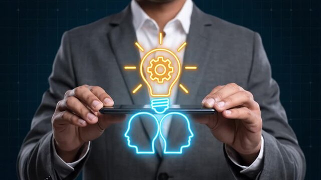 A businessman in a grey suit lifting a smartphone that projects a glowing hologram of two faces sharing a light bulb with a gear inside