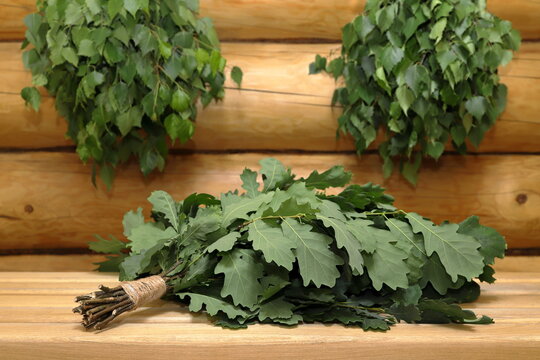 A fresh bath brooms, made from birch and oak branches, hang on a log wall and stand on a plank bench in the sauna.