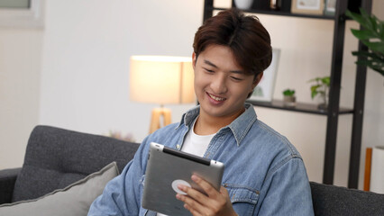 Smiling Young Asian Man Using Tablet Computer on Living Room Sofa © blueringmedia