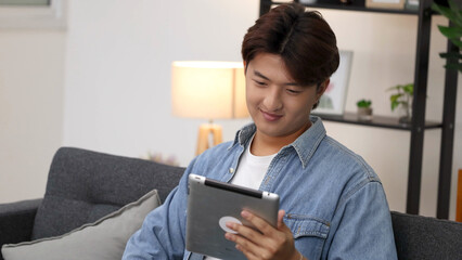 Smiling Young Asian Man Using Tablet Computer on Living Room Sofa © blueringmedia