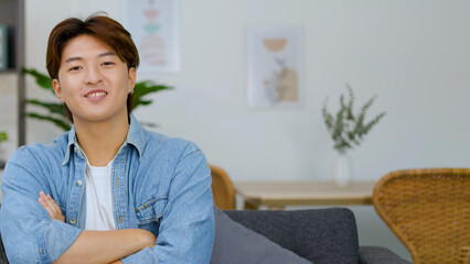 Obraz premium Smiling Young Asian Man with Arms Crossed in Bright Living Room