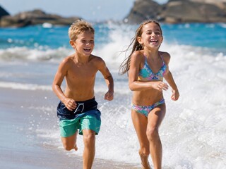 Fototapeta premium Two Happy Young Children Running and Laughing through Ocean Waves on a Sunny Tropical Beach for Family Travel and Summer Vacation Lifestyle