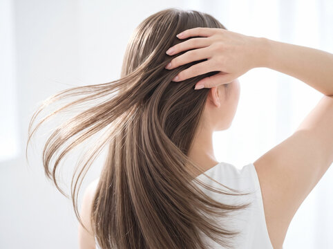 指先で優しく毛流れを整えて風をはらむロングヘアの後ろ姿の女性