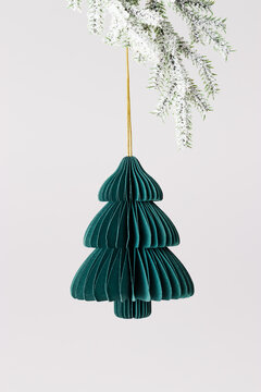Minimalist Christmas tree ornament folded green paper hanging on golden string on snowy pine branches on light gray background. Stylish eco-friendly New year festive decor in Scandinavian design.