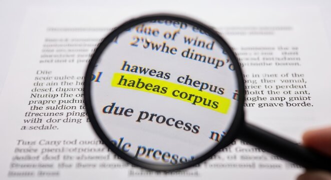 A magnifying glass highlights the Latin phrase habeas corpus on a legal document in a quiet library setting.