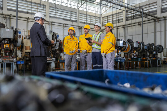 Manufacturing manager leading a daily production meeting with engineers and factory technicians on an industrial shop floor before production activities.