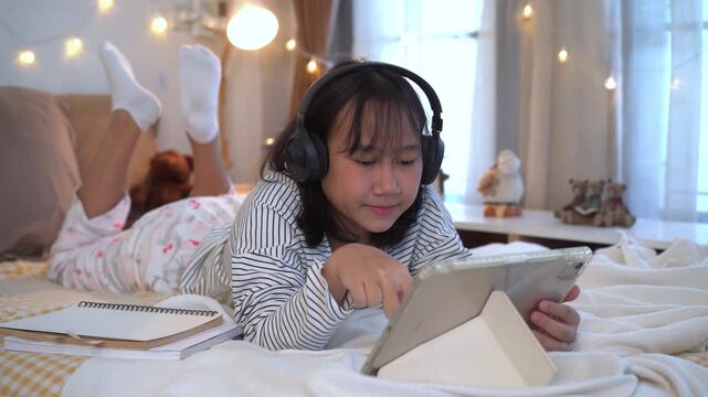 Relaxing Evening, Young girl wearing headphones lies comfortably on bed using a tablet in a warm, cozy bedroom decorated with soft fairy lights