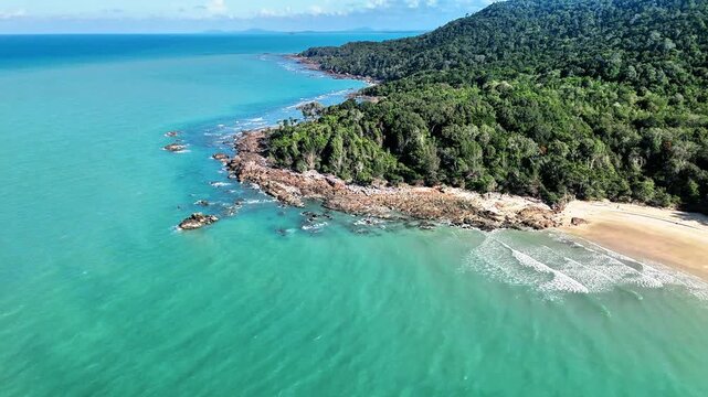 Aerial drone view of a hidden tropical beach with turquoise ocean, lush green hills, granite shoreline and untouched coastal paradise landscape below