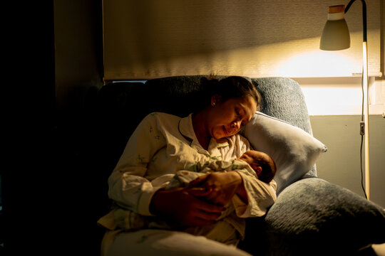 Mother Holding and Looking Lovingly at Her Sleeping Newborn Baby under Warm Lamp Light