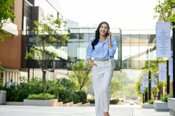 Fototapeta premium Asian young businesswoman talking on smartphone while walking in city. 