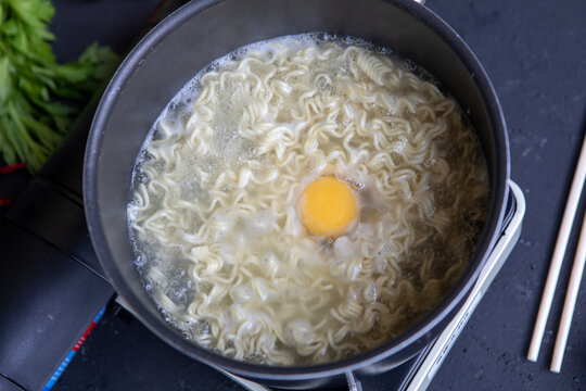 Cooking Instant Ramen Noodles with Raw Egg in Boiling Pot, Top View
