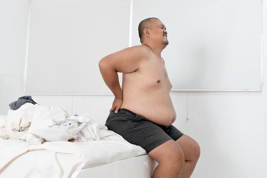 Overweight Asian Man Suffering from Severe Lower Back Pain on Bed