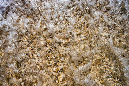Foamy seawater washing over a pebble beach on the Adriatic coast of the Marche region, Italy, creating a natural background with dynamic texture and motion