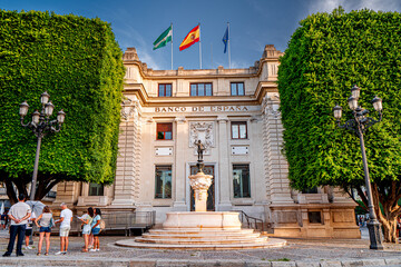 People in front of Bank of Spain in Seville, city square with flags Spain, Andalusia and European Union. Life on streets Spanish city. © Tomasz