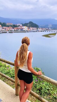 Woman looking at coastal town and river estuary from viewpoint, Ribadesella, Asturias, Spain