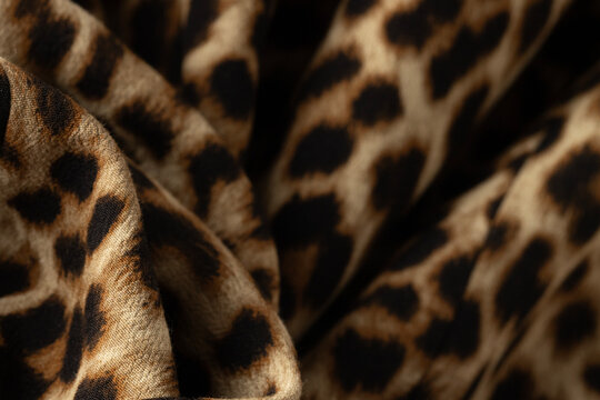 A dynamic, close-up view of a leopard print fabric with natural, earthy tones and black spots. 