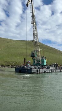 A large dredger boat with an excavator bucket performs dredging operations on a river in Olkhonsky District, Irkutsk Oblast, Russia