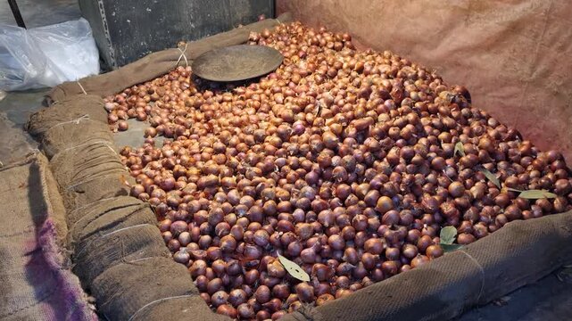 Indoor scene at a bazaar in Old Dhaka, Bangladesh, showing a large quantity of red onions neatly arranged for sale, capturing everyday market life and local trade activity