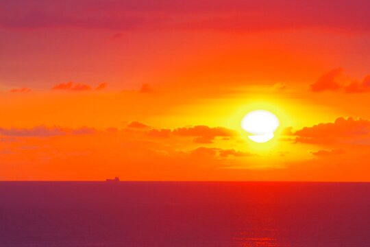 Fiery sunset over sea with cargo ship silhouette and copy space