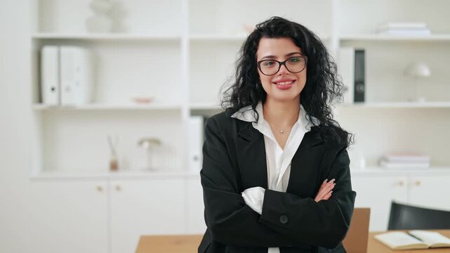 Confident business woman stands in professional office, arms crossed. Positive demeanor conveys happiness success. Smart attire suitable for corporate environments, leadership and ambitious career.