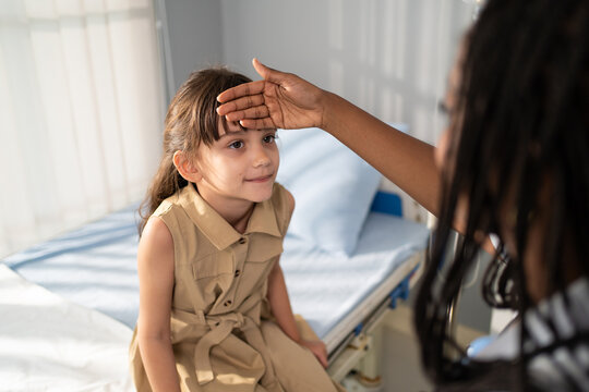 African pediatrician examining young girl during medical checkup in hospital. 