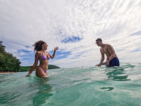 Young loving couple plays together in the ocean water near the shore.
