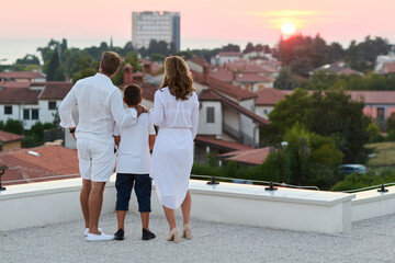 Obraz premium Family Watching Sunset Over Coastal Town From Rooftop Terrace Balcony With Sea View