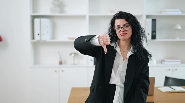 Upset businesswoman giving thumbs down, expressing disapproval, failure, or bad results. Corporate lifestyle, negative feedback and career problem concept in contemporary workspace