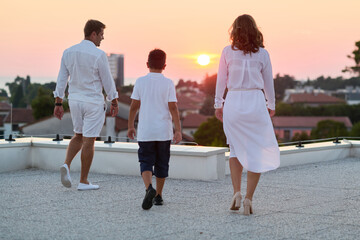 Obraz premium Family Walking On Rooftop Terrace At Sunset With Sea View — Parents And Child Together