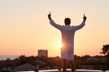 Obraz premium Man Celebrating on Rooftop Balcony at Sunset With Sea View Over Coastal Town