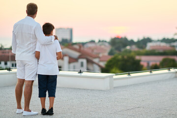 Obraz premium Father And Son On Rooftop Balcony Overlooking Sea View At Sunset Family Moment Together