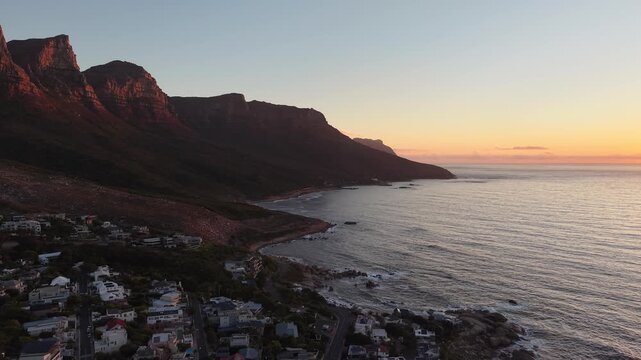 Aerial drone view over Camps Bay, Cape Town, at sunset. The Atlantic coastline, golden evening light and Lion's Head in the background create one of South Africa's most iconic coastal landscapes.