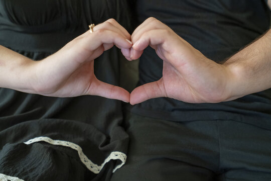 Couple forming a heart shape with their hands, symbolizing love and connection in a cozy setting.
