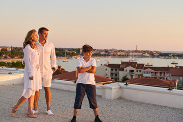 Obraz premium Family on Rooftop Terrace With Sea View at Sunset — Summer Vacation Balcony Overlooking Harbor Town