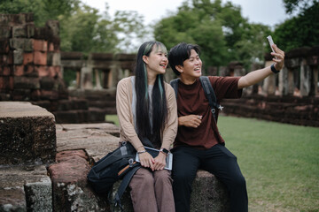 Obraz premium Young Asian Travelers Taking Smartphone Selfie While Exploring Historic Temple with Copy Space