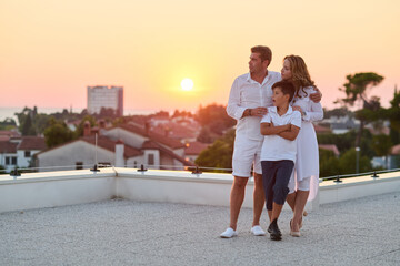 Obraz premium Family On Rooftop Balcony At Sunset With Sea View Enjoying Summer Vacation Together
