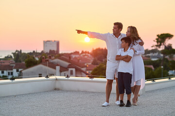 Obraz premium Family on Rooftop Terrace at Sunset Overlooking Sea View and Coastal Town