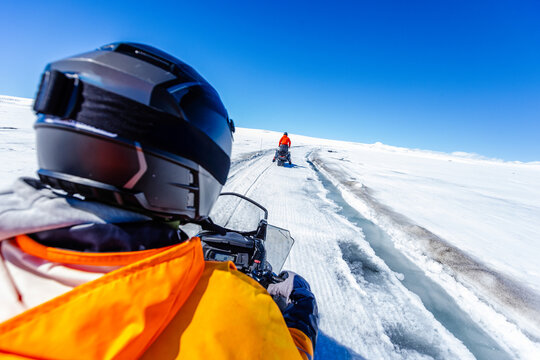 First-person view of a snowmobile tour across a vast Icelandic glacier. Adventure travel through pristine snowfields beneath a dramatic blue sky with wispy clouds in Iceland.