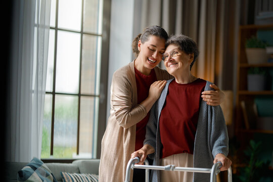 Happy Young Caregiver Embracing Senior Woman Using Walker at Home