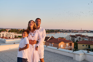 Obraz premium Happy Family On Rooftop Terrace With Sea View At Sunset Over Coastal Town