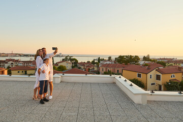 Obraz premium Family Taking Selfie on Rooftop Terrace With Sea View at Sunset During Vacation