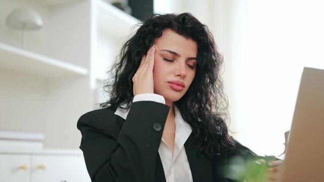 Young professional experiences severe headache at office. Exhaustion and stress contribute to discomfort while working on laptop. Feeling overwhelmed and unwell, seeking relief from pain.
