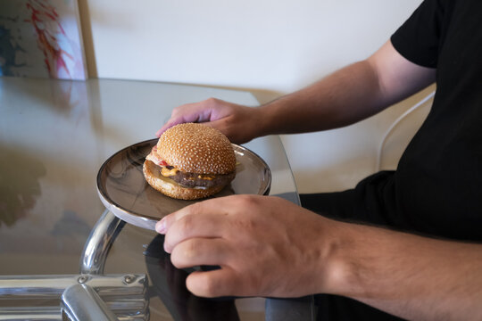 Person holding a delicious hamburger on a plate, ready to enjoy a flavorful meal at home.