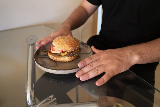 Man holding a delicious burger on a stylish plate, ready to enjoy a meal in a modern setting.