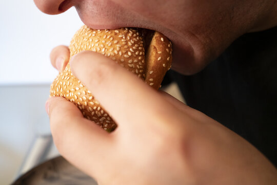 Close-up of a person biting into a sesame seed bun, showcasing the texture and detail of the food and hand.